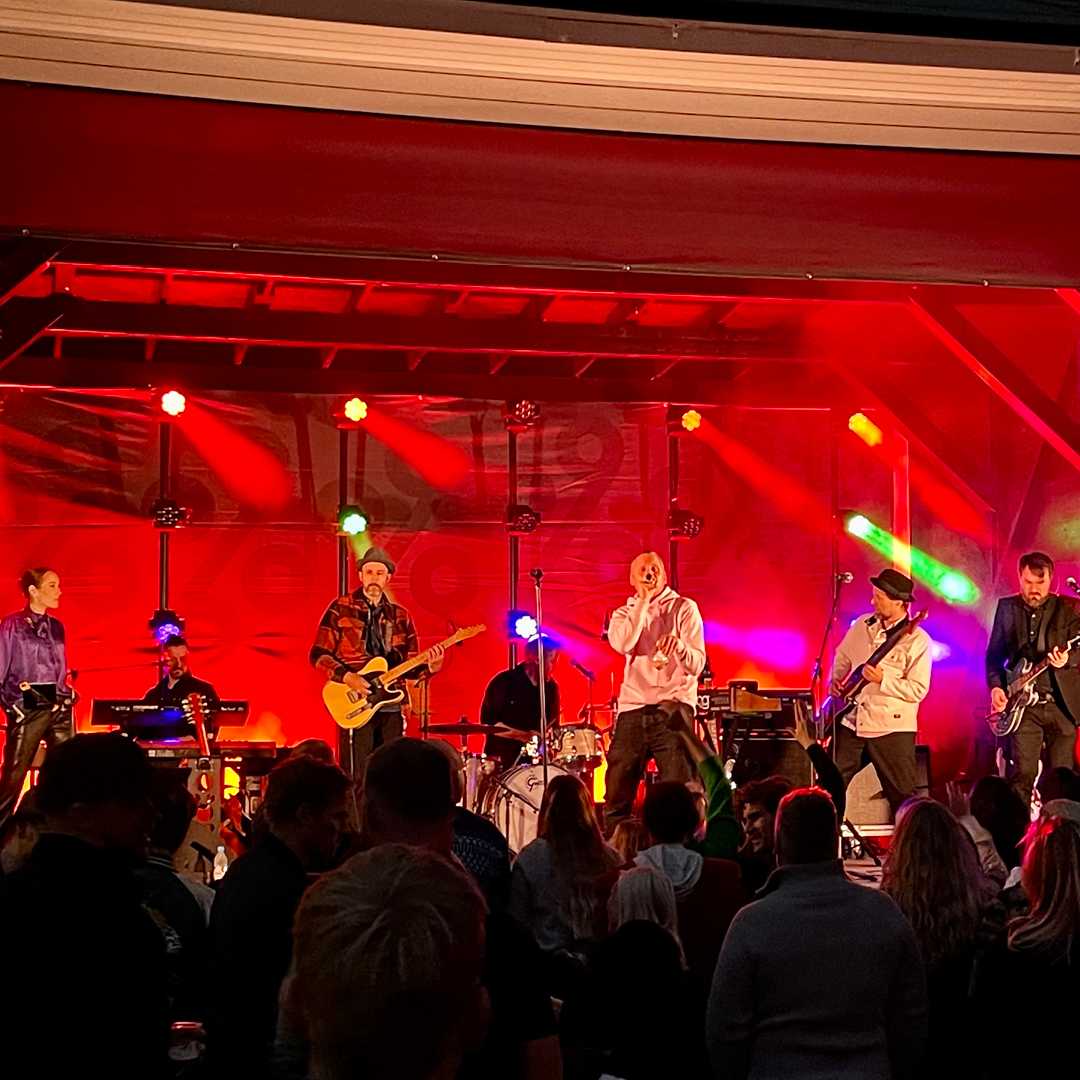 Festivalband spiller live på scenen med fargerik lyssetting – Medvind Eventbyrå